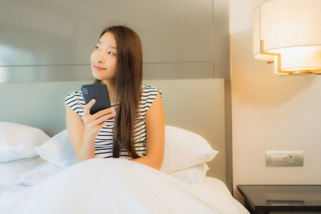 Portrait beautiful young asian woman use smart mobile phone on bed in bedroom interior