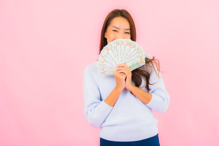 Portrait beautiful young asian woman with a lot of cash and money on pink color backgroundの写真素材