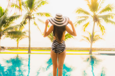 Portrait beautiful young asian woman relax around outdoor swimming pool in hotel resort with palm tree at sunset or sunrise for leisure vacationの写真素材
