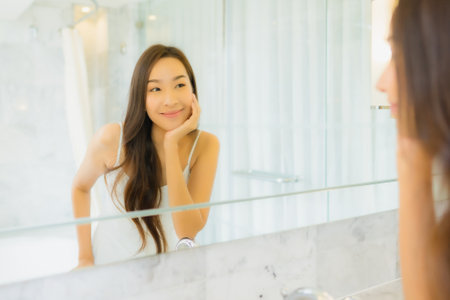 Portrait beautiful young asian woman check up and make up her face on mirror in bathroom interiorの写真素材