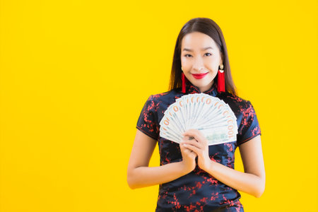 Portrait beautiful young asian woman wear chinese dress with a lot of cash or money for chinese new year concept on yellow isolated backgroundの写真素材