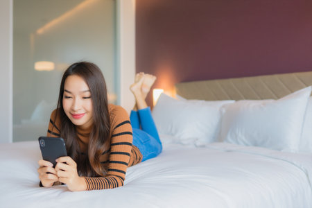 Portrait beautiful young asian woman use smart mobile phone on bed in bedroom interiorの写真素材