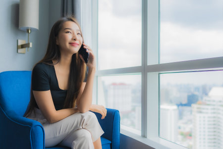 Portrait beautiful young asian woman use smart mobile phone on sofa in living room areaの写真素材