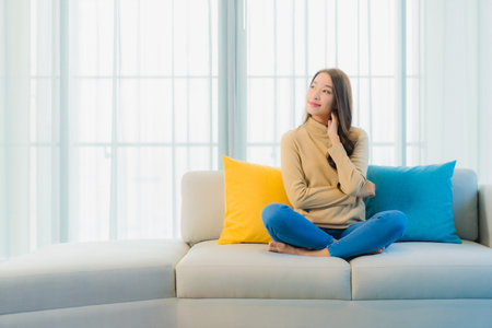 Portrait beautiful young asian woman relax leisure enjoy on sofa in living room interior areaの写真素材