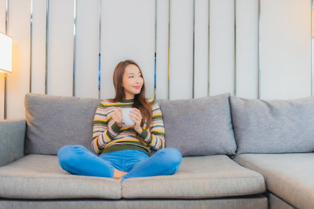 Portrait beautiful young asian woman sit smile relax on sofa in living room interiorの写真素材
