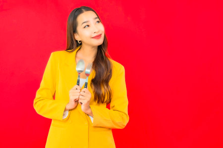 Portrait beautiful young business asian woman with spoon and fork on red backgroundの写真素材