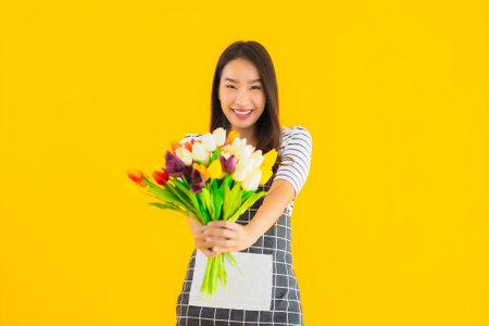Portrait Beautiful young asian woman wear apron with colorful flower or floral on yellow backgroundの写真素材