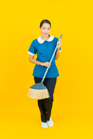 Portrait beautiful young asian woman maid and housekeeping smile with action on yellow color backgroundの写真素材