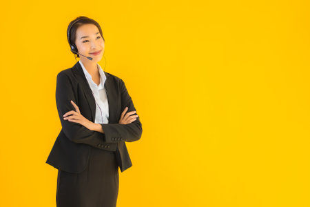 Portrait beautiful young business asian woman with headphone or headset for call center or telemarketing on yellow isolated backgroundの写真素材