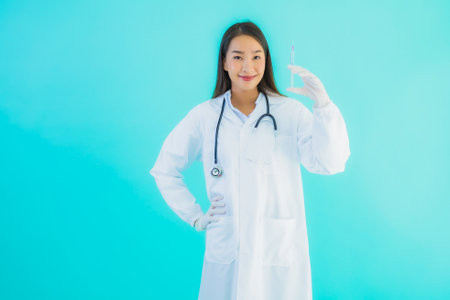 Portrait beautiful young asian doctor woman with syringe injection on blue isolated backgroundの写真素材