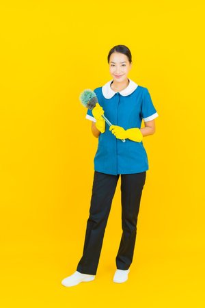 Portrait beautiful young asian woman maid and housekeeping smile with action on yellow color backgroundの写真素材