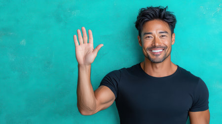 A Friendly Asian man waving with bright teal background, showcasing warmth and positivityの素材