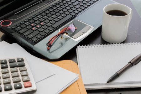 Closeup Coffee cup, laptop, Document file , pen , Calculator , notepad and glasses on wooden tableの写真素材