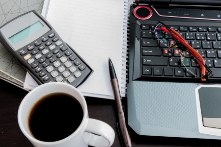 Closeup Coffee cup, laptop, Document file , pen , Calculator , notepad and glasses on wooden tableの写真素材