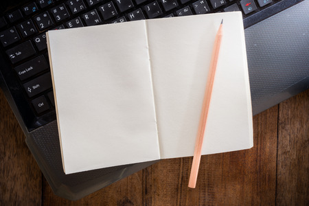 Blank notebook with pencil on Laptop and wooden table. The view from the top
