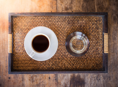 Cup of coffee on a wooden table with glass of water in the wooden tray. The view from the topの写真素材