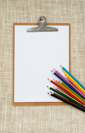 wooden clipboard and colored pencils on old sackcloth background, with regular white blank paper.の写真素材