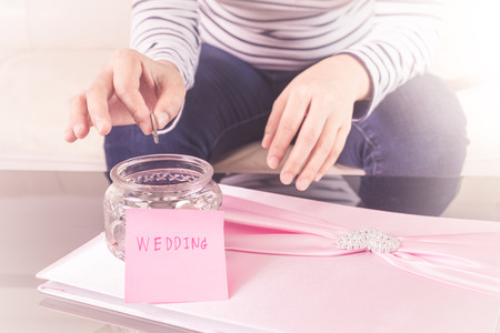 Hand putting a coin into glass jars with 'wedding' text. wedding concept , saving concept. focus at hand hold coinの写真素材