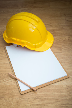 Yellow Safety Helmet Hat and clipboard and pencil on Wood backgroundの写真素材