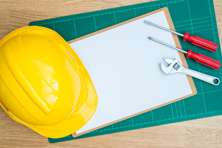 Yellow Safety Helmet Hat and clipboard , Cutting pads, screwdriver,wrench on Wood backgroundの写真素材