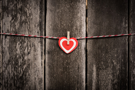Red paper heart hanging on the clothesline. On old wood background. Valentine Concept