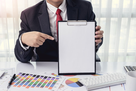 Business man Showing a blank paper (space for your text) at office with desktop computer and documents on his desk, consultant lawyer conceptの写真素材