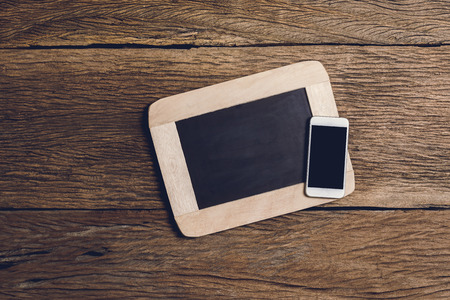 Vintage slate chalk board and smartphone on wooden background. Concept of communication technology from the past to the sub-Present.の写真素材