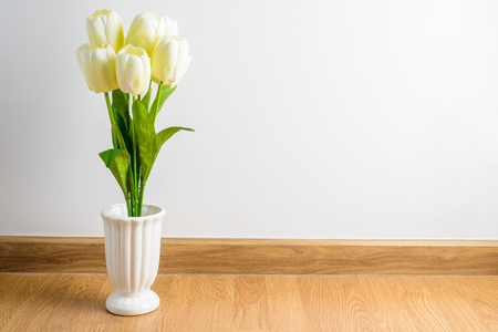 white tulip flowers bouquet in vase on wooden floor in front of cement wall. View with copy spaceの写真素材