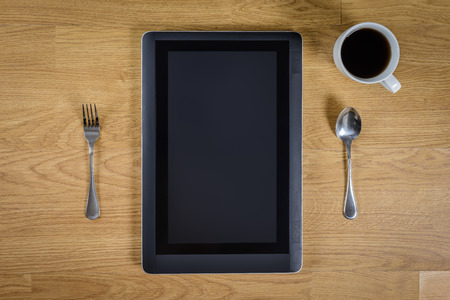 blank digital tablet over wood table with spoon, fork and coffee cupの写真素材