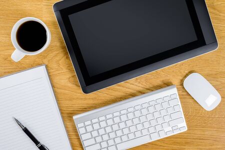 mans working place at wooden desktop with coffee. Office desk table with keyboard, tablet, notebook, cup of coffee. Top view with copy spaceの写真素材