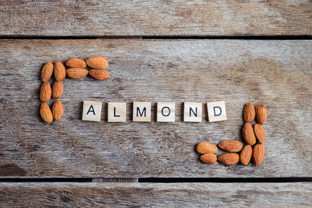 the word "ALMOND" of the wooden letter blocks with Peeled almonds closeup on against dark rustic wooden background. For vegetariansの写真素材