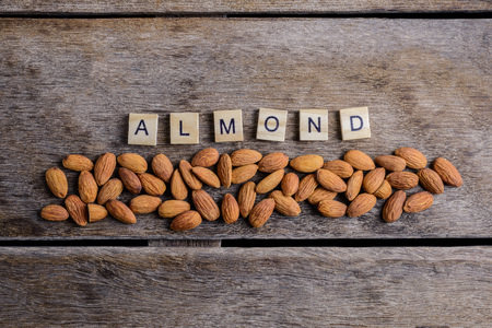 the word "ALMOND" of the wooden letter blocks with Peeled almonds closeup on against dark rustic wooden background. For vegetariansの写真素材