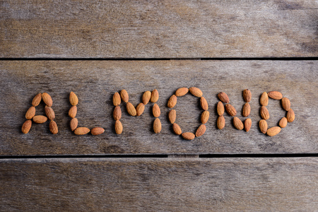 the word "ALMOND" array with Peeled almonds closeup on against dark rustic wooden background. For vegetariansの写真素材