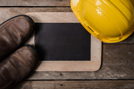 Yellow protective safety helmet, Safety shoes with chalkboard on old wooden background. safety first conceptsの写真素材
