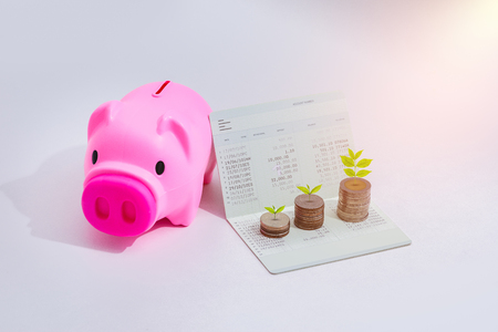 stack of coins with piggy bank and account book bank on the table in saving, banking and finance conceptの写真素材