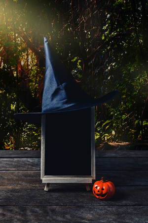 Halloween background. Spooky pumpkin, Witch hat, chalkboard on wooden floor with moon and dark forest. Halloween design with copyspaceの写真素材