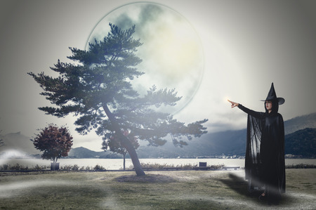 Portrait of woman in black Scary witch halloween costume with moonlight in a dark forestの写真素材