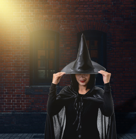 Portrait of woman in black Scary witch halloween costume with Brick Wall of the Ancient Castle of...