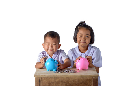 Cute asian country boy and girl in school uniform putting coins into piggy bank isolated on white background  . Education Savings conceptsの写真素材