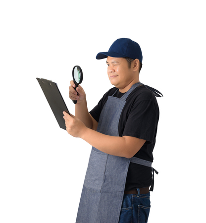 worker man or Serviceman in Black shirt and apron is holding clipboard and use Magnifying glass isolated on white background with clipping pathの写真素材