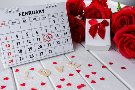 Calendar page with red hand written heart highlight on February 14 of Saint Valentines day with red rose and red Heart shape, Gift box, Wooden letters word "LOVE" on white wooden tableの写真素材