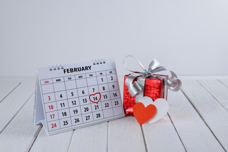 Calendar page with red hand written heart highlight on February 14 of Saint Valentines day with red gift box and Heart shape on white wooden tableの写真素材