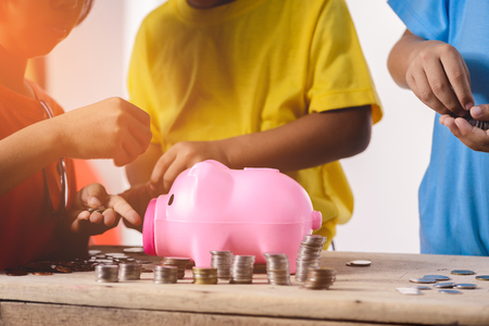 Hands of asian children are helping putting coins into piggy bank on white background. Education Savings conceptsの写真素材