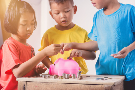 Group Of Asian Children Are Helping Putting Coins Into Piggy Bank