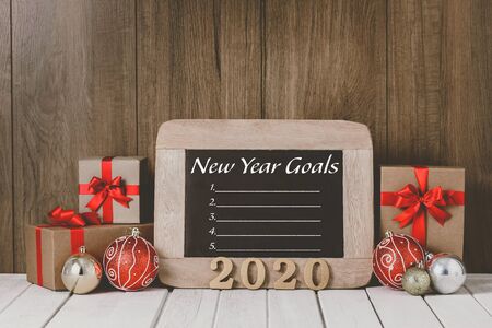 2020 wooden text and Christmas ornaments, gift boxes and New Year's Goals List written on chalkboard...