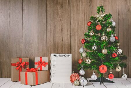 christmas tree with colorful balls ornaments and gift boxes and New Year's Goals List written on Notebook with copy spaceの写真素材