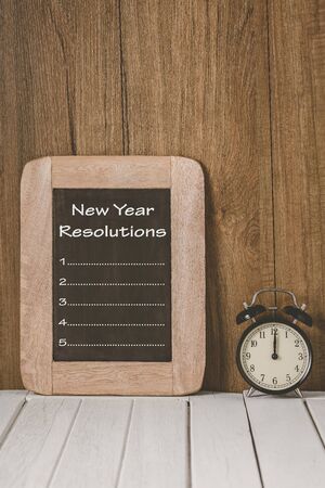 New Year's Resolutions List written on chalkboard with Alarm clock over wooden backgroundの写真素材