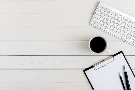 Flat lay, top view wooden office desk. Workspace with blank clipboard, keyboard, pen, coffee cup office supplies with coppy space on white wood table backgroundの写真素材