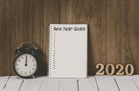 2020 wooden text and New Year's Goals List written on Notebook with Alarm clock over wooden backgroundの写真素材