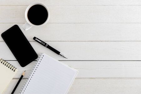 Flat lay, top view wooden office desk. Workspace with blank notebook, smartphone, pen, coffee cup office supplies with coppy space on white wood table backgroundの写真素材